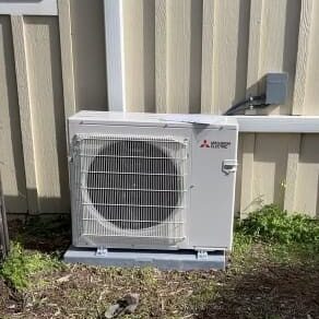 A white air conditioner sitting outside of a house.